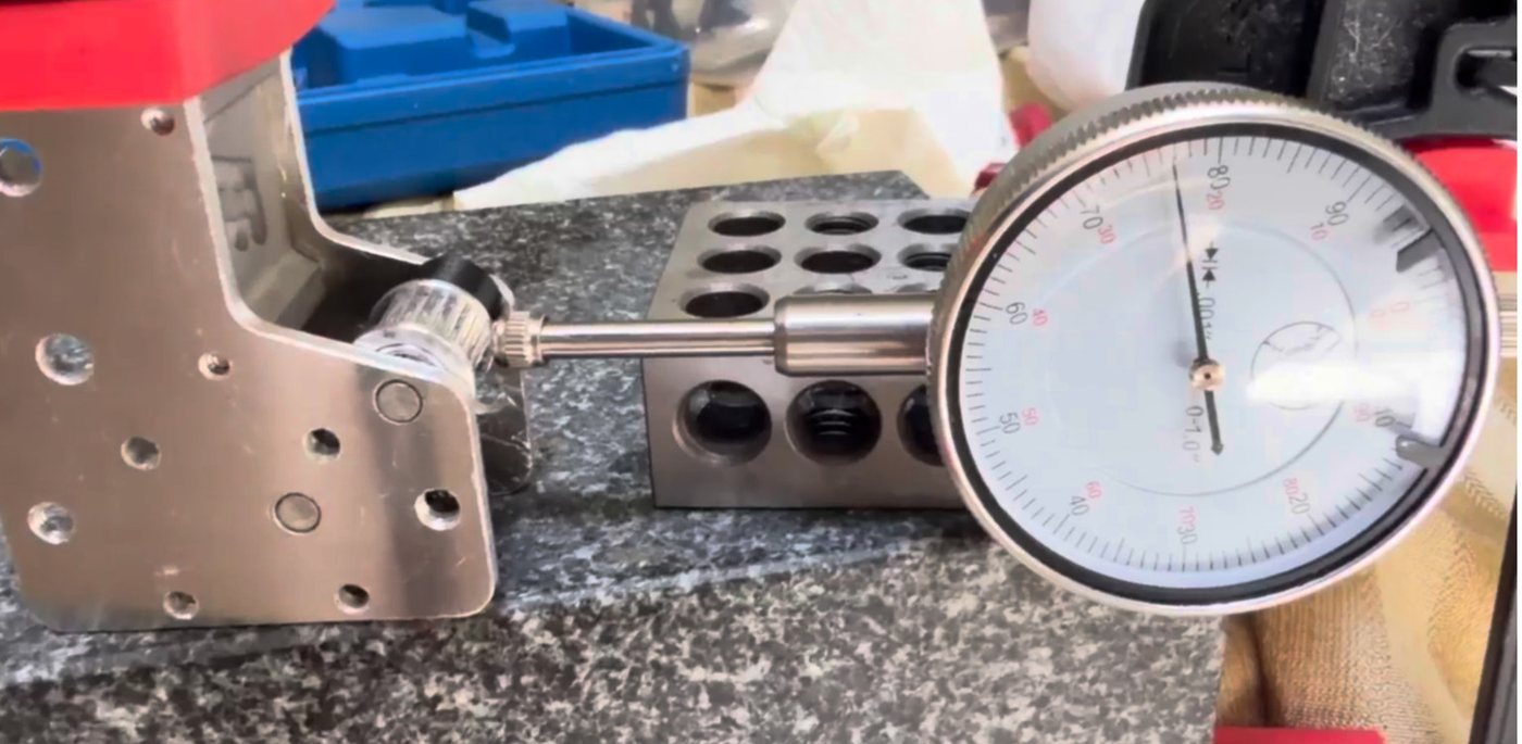 A dial indicator reading the face of a pressed idler, with the assembly squared between granite blocks.